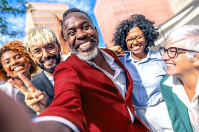 Ljudi različitog uzrasta, rase i pola koji se široko smeju ispred zgrade